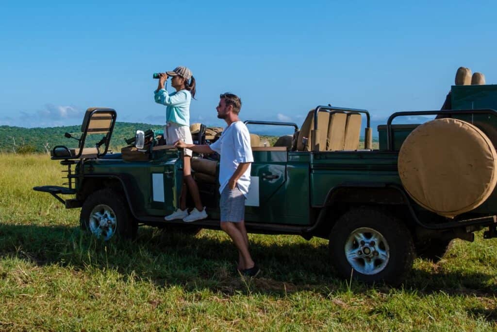 A young couple on safari, looking out over the savannah from their safari vehicle