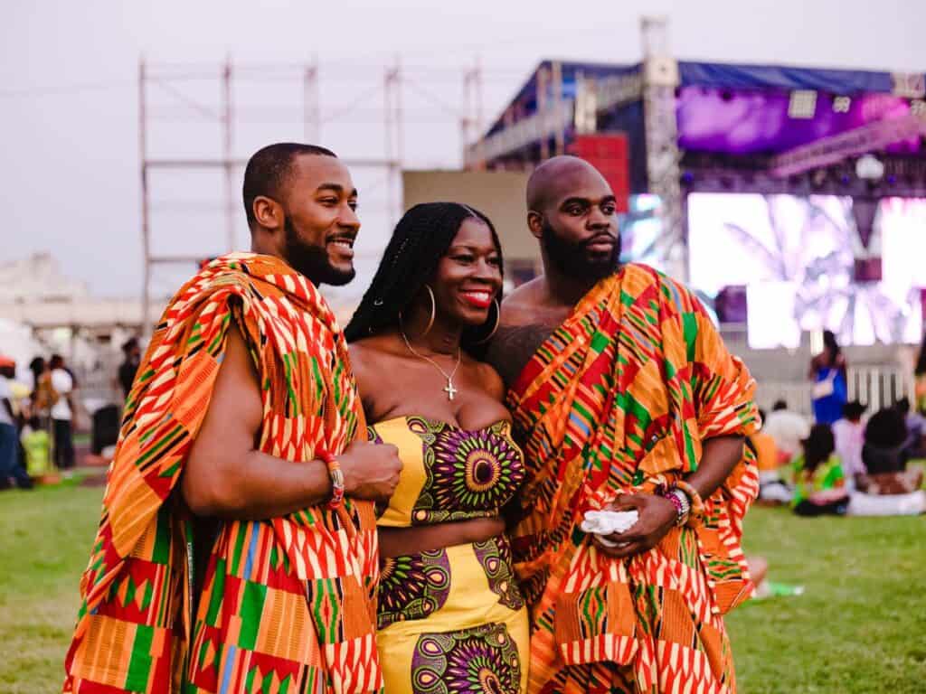 Attendees to a music festival in Ghana, 2 men and a women in traditional clothing